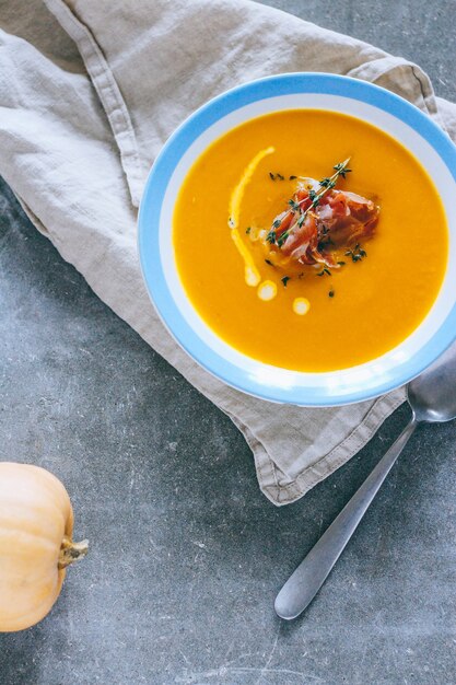 Un piatto di zuppa di zucca con un jamon, aglio, timo e crema, su uno sfondo grigio