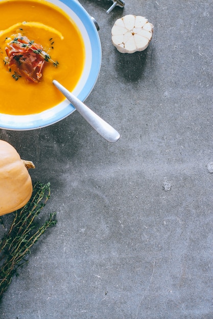 Un piatto di zuppa di zucca con un jamon, aglio, timo e crema, su uno sfondo grigio