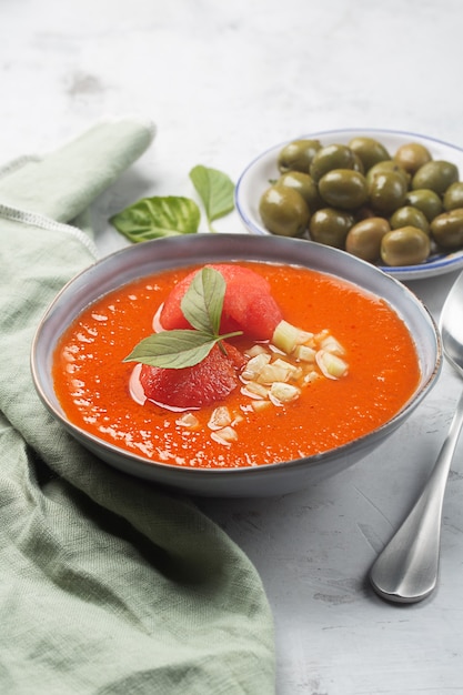 Un piatto di zuppa fredda sotto forma di purè di gazpacho e olive con un cucchiaio. Piatto tradizionale spagnolo di pomodori equilibrati, peperoni, aglio con un tovagliolo color oliva