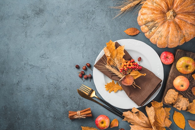 Un piatto posate foglie autunnali mele e una zucca su uno sfondo grigio blu scuro