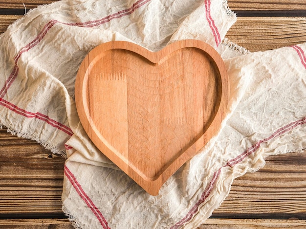Un piatto vuoto a forma di cuore con un tovagliolo da cucina si trova su un tavolo di legno con spazio per il testo nella vista centrale dall'alto