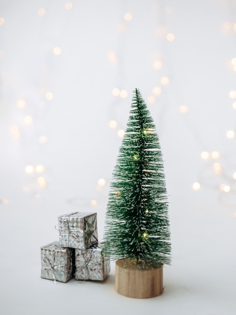 Un piccolo albero di Natale artificiale con regali su uno sfondo bianco con una ghirlanda con un posto per il testo