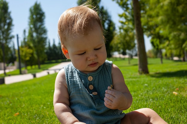 Un piccolo bambino si siede sull'erba del parco e studia i fili d'erba gioca con l'erbaEstate e il sole splendenteUna passeggiata all'aria aperta