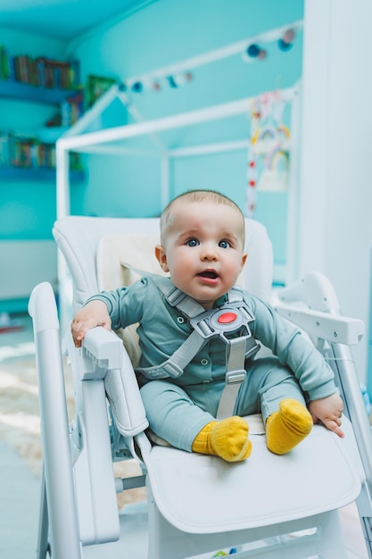 Un piccolo bel ragazzo è seduto su un seggiolone per l'alimentazione Sedia da cucina per bambini per mangiare Mobili per bambini