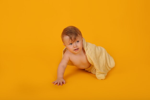 un piccolo bellissimo ragazzo con il blu coperto da un asciugamano striscia su uno studio di sfondo giallo