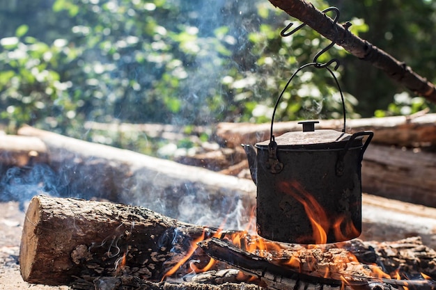 Un piccolo bollitore con acqua viene riscaldato su un fuoco in una foresta in una giornata di sole estivo