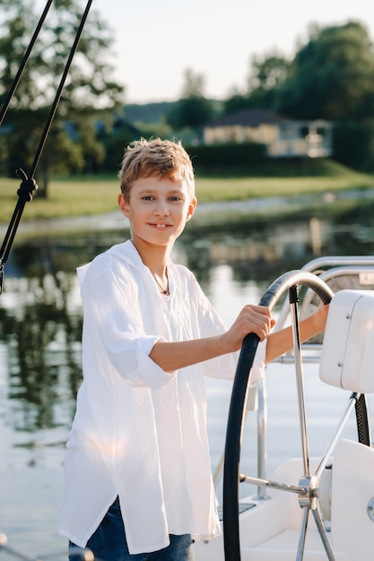 Un piccolo capitano al timone di uno yacht. un ragazzino al timone del capitano su uno yacht al tramonto.