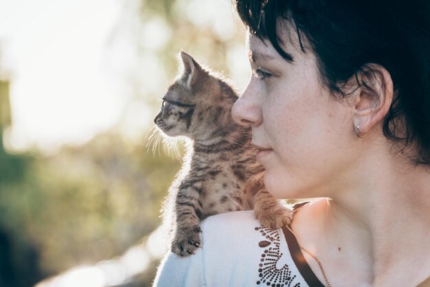 Un piccolo gattino seduto sulla spalla di una ragazza durante una passeggiata