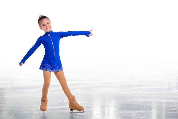 Un piccolo giovane pattinatore in posa in abito da allenamento blu su ghiaccio che mostra gesto di successo isolato su sfondo bianco