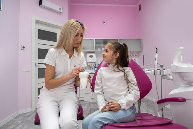 un piccolo paziente si siede sulla sedia del dentista dove il dentista le dice come lavarsi i denti correttamente