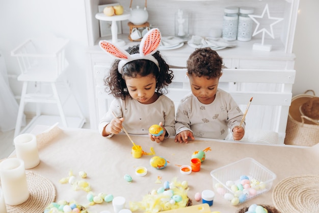 Un piccolo ragazzo e una ragazza afroamericani dipingono le uova di Pasqua a casa i bambini neri si stanno preparando per la Pasqua