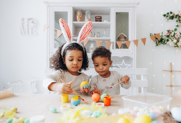 Un piccolo ragazzo e una ragazza afroamericani dipingono le uova di Pasqua a casa i bambini neri si stanno preparando per la Pasqua