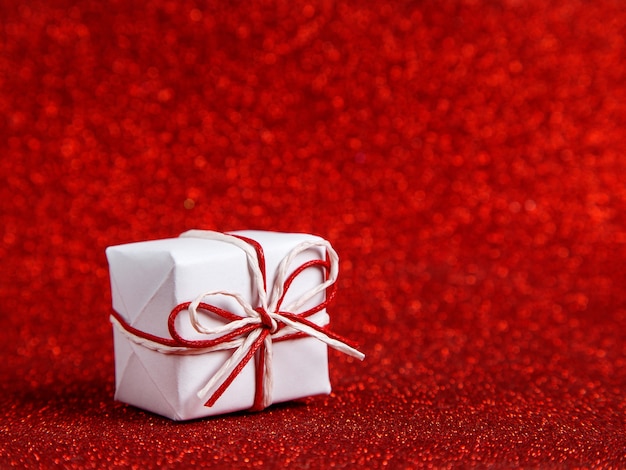 Un piccolo regalo bianco su un rosso lucido, paillettes sul lato. Il concetto per il giorno di San Valentino.