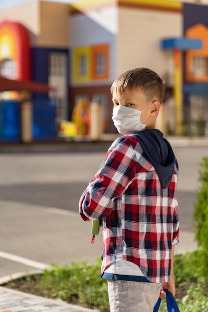 Un piccolo scolaro con una maschera medica va a scuola.