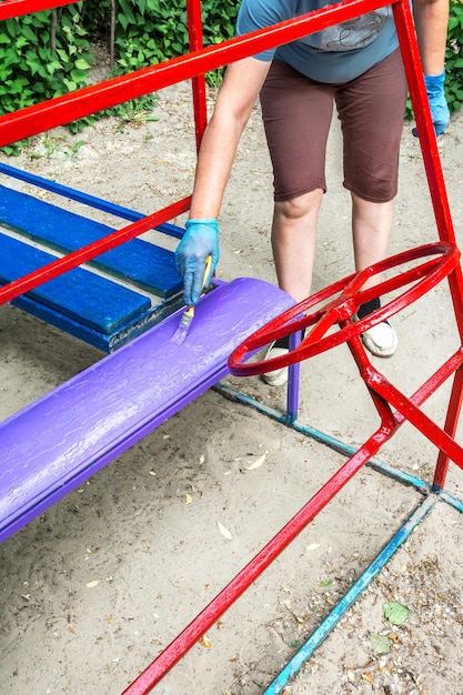 Un pittore dipinge una panca di legno con lo smalto nel parco giochi dell'asilo