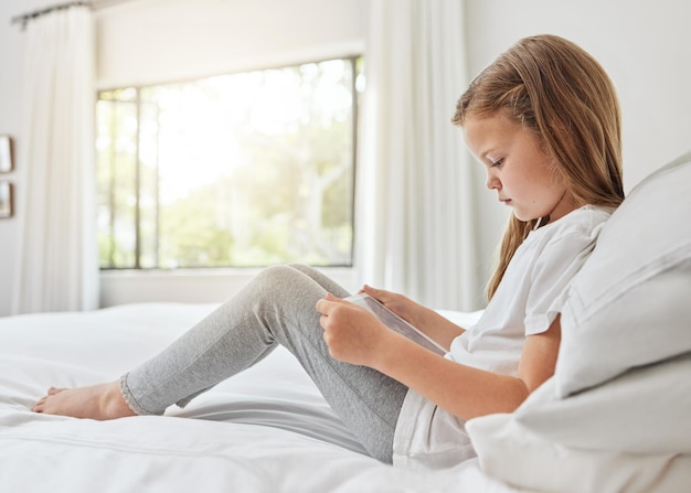 È un po' introversa. Inquadratura di una bambina che usa una tavoletta digitale a letto a casa.