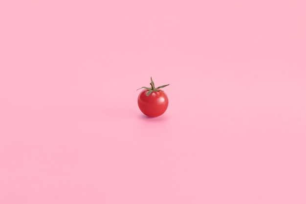 Un pomodoro ciliegino su sfondo rosa