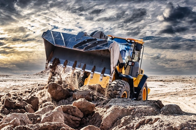 Un potente bulldozer o caricatore sposta la terra nel cantiere contro il cielo Una macchina per movimento terra sta livellando il sito Costruzione di attrezzature pesanti per lavori di sterro