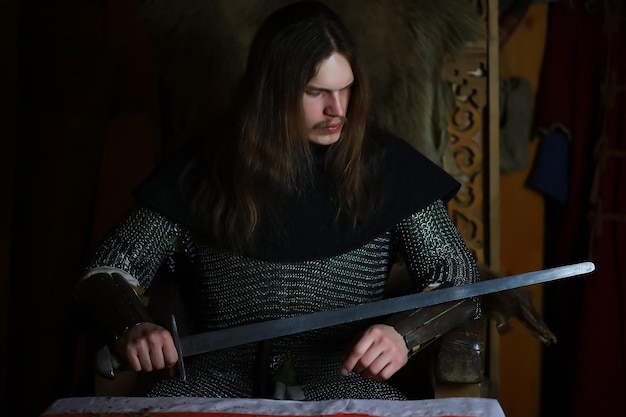 Un potente eroe con i capelli lunghi in armatura di cotta di maglia in un'antica sala. Guerriero medievale nelle camere del cavaliere.