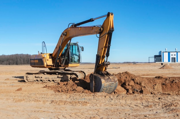 Un potente escavatore a cingoli scava il terreno contro il cielo blu Lavori di sterro con attrezzature pesanti in cantiere