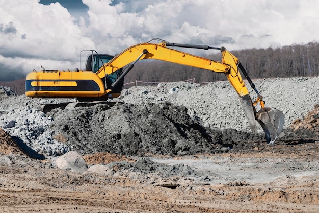 Un potente escavatore scava il terreno contro il cielo blu Lavori di sterro con attrezzature pesanti in cantiere