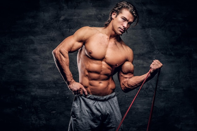 Un potente uomo muscoloso sta facendo esercizi con la gomma e mostra i suoi muscoli.