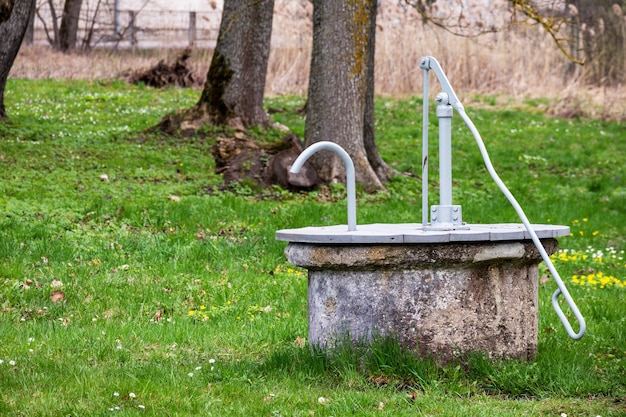 Un pozzo d'acqua in un campo con alberi sullo sfondo.