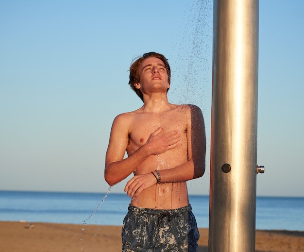 Un primo piano del giovane che fa la doccia sulla spiaggia.