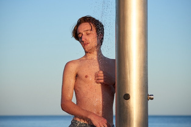 Un primo piano del giovane che fa la doccia sulla spiaggia.