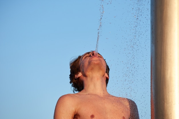 Un primo piano del giovane uomo nudo che getta acqua dalla bocca