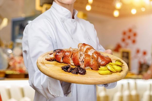 Un primo piano del vassoio della tenuta del capo cuoco con una combinazione di patate di carne preparate e frutta secca su di esso sullo sfondo sfocato dell'interno del ristorante