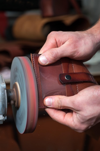 Un primo piano di un artigiano lavora con la levigatura dei bordi di un portafoglio nella produzione di articoli in pelle