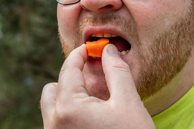 Un primo piano di un maschio adulto con la barba che mangia una carota tagliata che raffigura un'alimentazione sana o uno spuntino