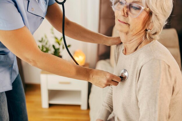 Un primo piano di un medico che fa un esame del cuore con una donna anziana durante la sua visita a casa