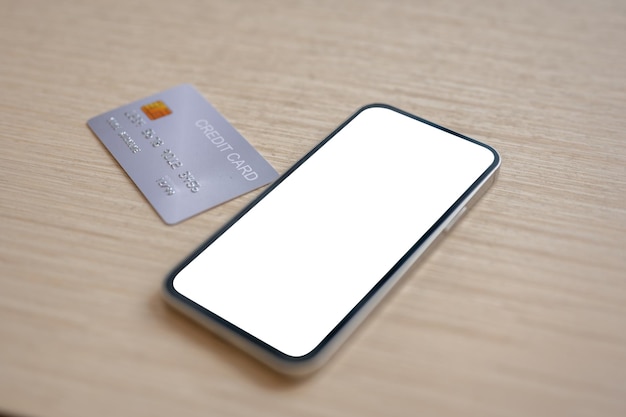 Un primo piano di una carta di credito e di uno smartphone con un modello di schermo bianco posto su un tavolo di legno all'interno
