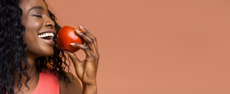 Foto un primo piano di una giovane donna nera con i capelli lunghi e ricci che morde un pomodoro rosso succoso
