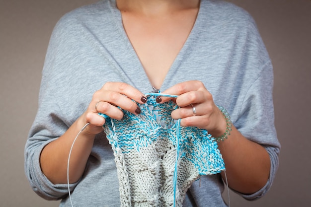 Un primo piano di una giovane donna sposata in un cardigan grigio lavora a maglia con ferri da maglia da fili di lana naturale un maglione a strisce bianche e blu