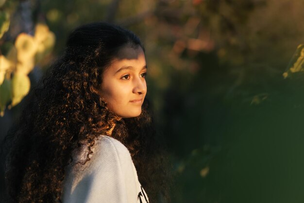 Un primo piano di una ragazza di 13 anni che guarda il tramonto attraverso gli alberi