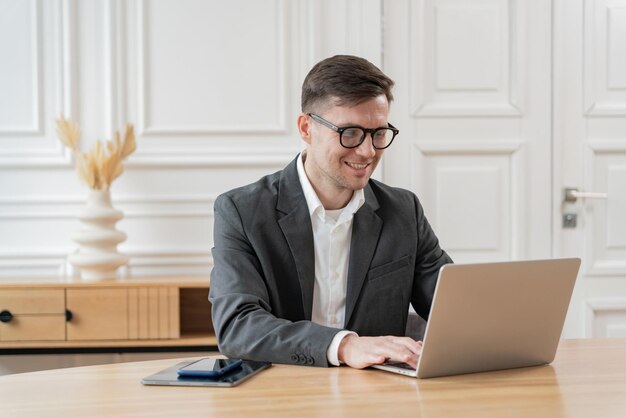 Un professionista d'affari con gli occhiali che lavora attentamente su un portatile mostra produttività e concentrazione in uno spazio d'ufficio luminoso