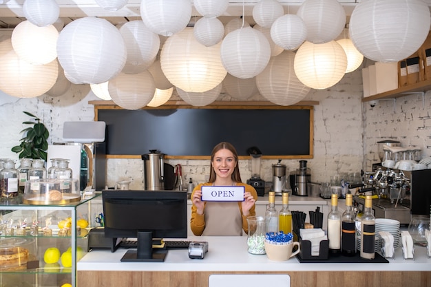 Un proprietario di caffè sorridente che tiene il segno aperto