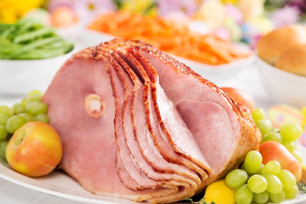 Un prosciutto tagliato a spirale con carote, fagiolini, pane e fiori di primavera per la cena di Pasqua