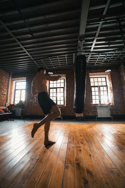 Un pugile atletico allenamento con un sacco da boxe in palestra Uomo che sta per calciare il sacco con una gamba