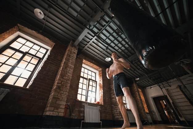 Un pugile uomo che si allena con un sacco da boxe in palestra