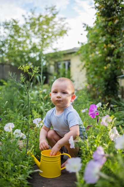 Un ragazzino aiutante è seduto in giardino con un annaffiatoio giallo