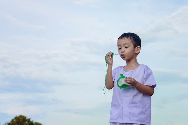 Un ragazzino asiatico che soffia bolle, giocando con gioia e felicità nella natura bella e verde.