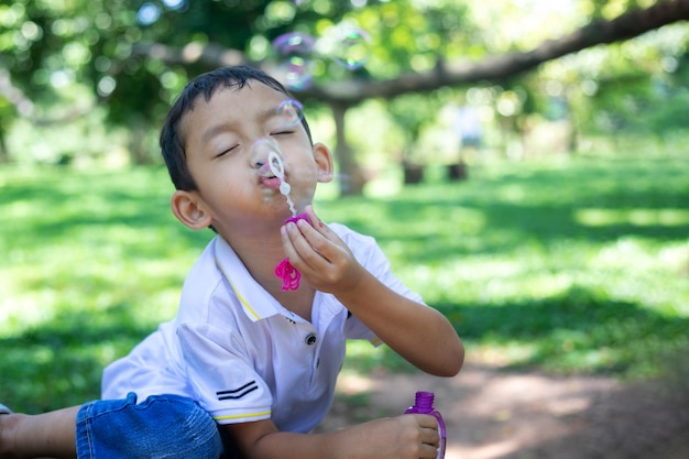 Un ragazzino asiatico che soffia bolle, giocando con gioia e felicità nella natura bella e verde.