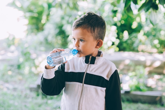 Un ragazzino beve acqua all'aperto da una bottiglia blu