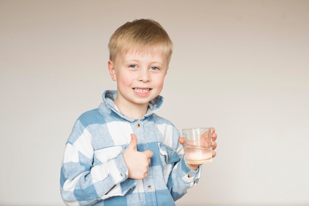 Un ragazzino beve acqua da un bicchiere su uno sfondo grigio nello studio