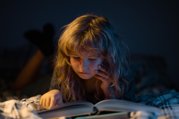 Un ragazzino carino che legge un libro sdraiato sul letto bambino che legge un libro sulla notte prima di coricarsi i bambini si sviluppano