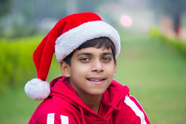 Un ragazzino carino con la maglietta rossa del berretto da Babbo Natale che sorride felicemente e guarda la telecamera